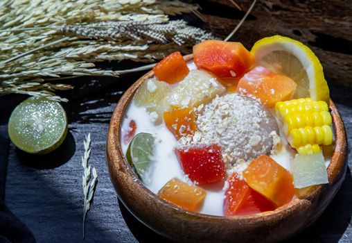 Tropical fresh fruit salad with milk and oatmeal on wooden bowl in dark background. Sweet healthy breakfast, Healthy vegan meal, Selective focus.