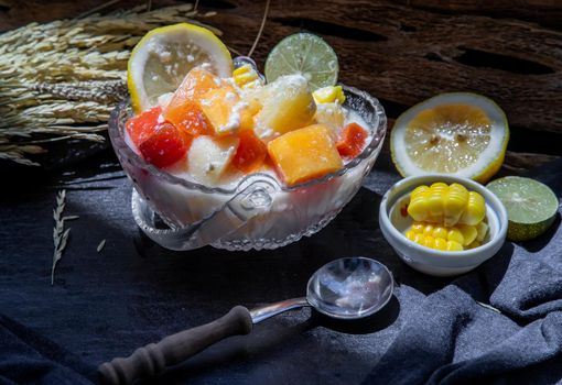 Tropical fresh fruit salad with milk and oatmeal  in a glass bowl served with corn on dark background. Sweet healthy breakfast, Healthy vegan meal. Selective focus.