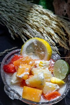 Tropical fresh fruit salad with milk and oatmeal in a glass bowl on dark background. Sweet healthy breakfast, Healthy vegan meal. Selective focus.
