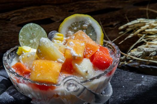 Tropical fresh fruit salad with milk and oatmeal in a glass bowl on dark background. Sweet healthy breakfast, Healthy vegan meal. Selective focus.