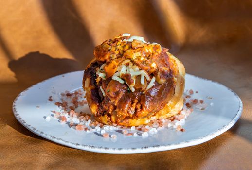 Homemade pizza buns topped with tomato sauce, ham, sausage, green onion and mozzarella cheese with himalayan pink salt on classic white plate.