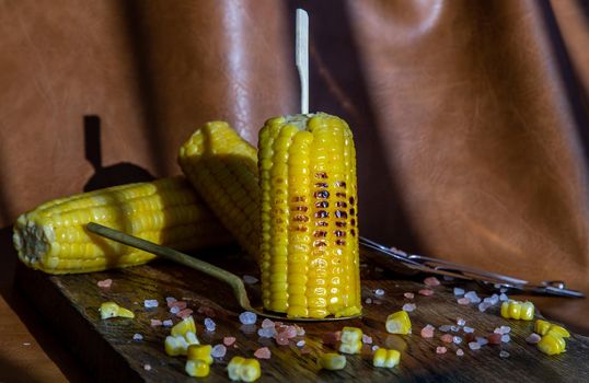 Grilled corn on the cob  on rustic wooden board over brown leather background.  Ideas for barbecue and grill parties, Barbecue concept.