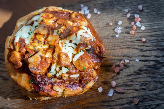 Homemade pizza buns topped with tomato sauce, ham, sausage, green onion and mozzarella cheese with himalayan pink salt on rustic wooden board.