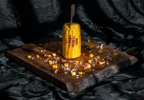 Grilled corn on the cob  on rustic wooden board   over dark background. Ideas for barbecue and grill parties, Barbecue concept.
