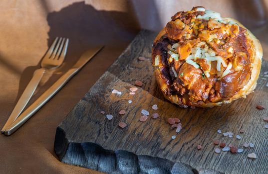 Homemade pizza buns topped with tomato sauce, ham, sausage, green onion and mozzarella cheese with himalayan pink salt on rustic wooden board.
