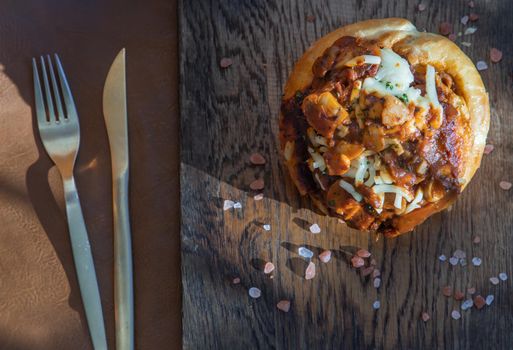Homemade pizza buns topped with tomato sauce, ham, sausage, green onion and mozzarella cheese with himalayan pink salt on rustic wooden board.