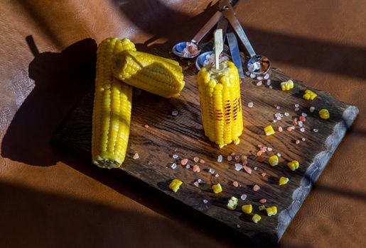 Grilled corn on the cob  on rustic wooden board over brown leather background.  Ideas for barbecue and grill parties, Barbecue concept.