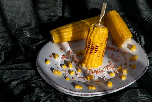 Grilled corn on the cob  on classic white plate over dark background. Ideas for barbecue and grill parties, Barbecue concept.