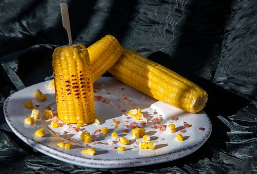 Grilled corn on the cob  on classic white plate over dark background. Ideas for barbecue and grill parties, Barbecue concept.