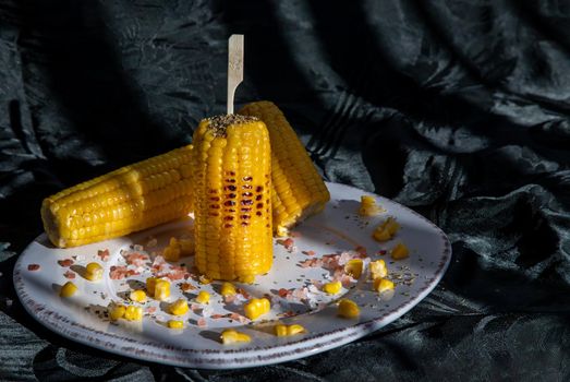 Grilled corn on the cob  on classic white plate over dark background. Ideas for barbecue and grill parties, Barbecue concept.