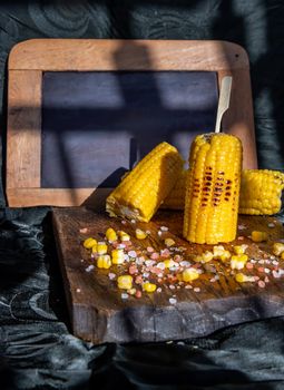 Grilled corn on the cob  on rustic wooden board   over dark background and Free space for text. Ideas for barbecue and grill parties, Barbecue concept.