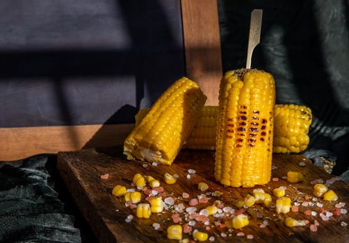 Grilled corn on the cob  on rustic wooden board   over dark background and Free space for text. Ideas for barbecue and grill parties, Barbecue concept.