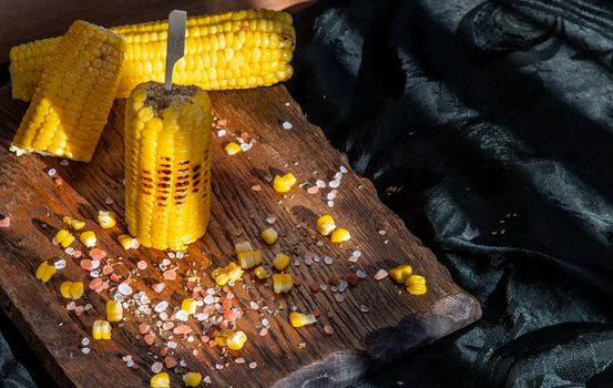 Grilled corn on the cob  on rustic wooden board   over dark background. Ideas for barbecue and grill parties, Barbecue concept.