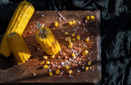 Grilled corn on the cob  on rustic wooden board   over dark background. Ideas for barbecue and grill parties, Barbecue concept.