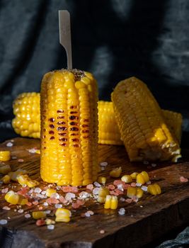 Grilled corn on the cob  on rustic wooden board   over dark background. Ideas for barbecue and grill parties, Barbecue concept.