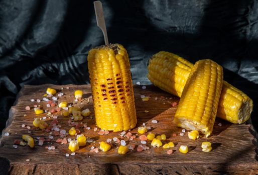 Grilled corn on the cob  on rustic wooden board   over dark background. Ideas for barbecue and grill parties, Barbecue concept.