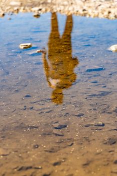 Silhouette of man reflecting in small puddle at sunny day