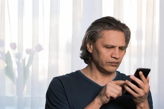 An adult gray-haired man is reading a text message on the phone. Concentrated. Close-up