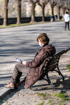 terni,italy march 25 2021:woman with medical mask sitting reading at the park