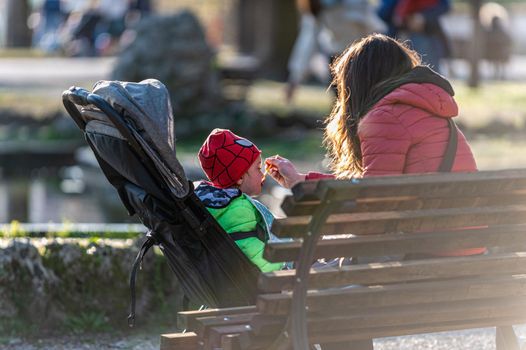 terni,italy march 25 2021:mom feeding her little son on the stroller at the park