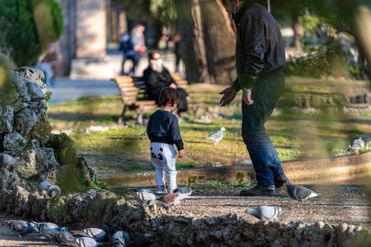 terni,italy march 25 2021:child at the park playing with pigeons near the fountain