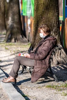 terni,italy march 25 2021:woman with medical mask sitting reading at the park