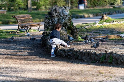 terni,italy march 25 2021:child at the park playing with pigeons near the fountain