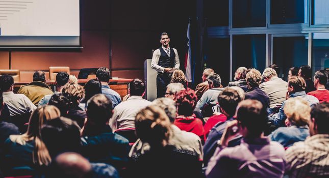 Speaker giving a talk in conference hall at business meeting event. Rear view of unrecognizable people in audience at the conference hall. Business and entrepreneurship concept.