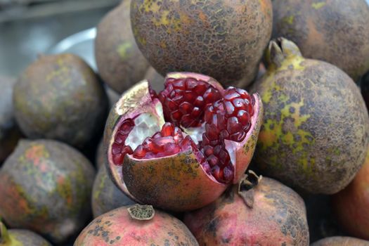 A closeup shot of an open ripe pomegranate in a market place, Pomegranate fruit stall for sale in market Delhi, India. The pomegranate is a fruit-bearing deciduous shrub in the family Lythraceae, subfamily Punicoideae.