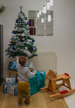 A cute redhead baby boy hanging blue baubles in a Christmas Tree