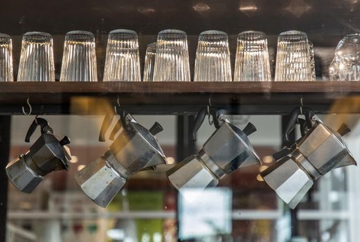 Interior design of coffee shop with glasses and moka pots. Moka pots are hanging on wooden rail. Selective focus
