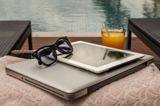 Relaxing moment by the pool. Take a break from working on laptop and tablet and enjoy the fresh orange juice for a refreshment.  Outdoor swimming pool background. leisure activity.