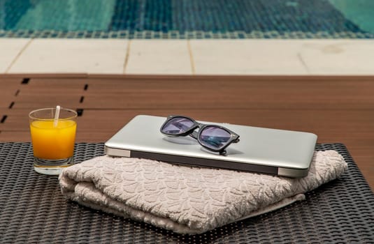 Relaxing moment by the pool. Take a break from working on laptop and enjoy the fresh orange juice for a refreshment.  Outdoor swimming pool background. leisure activity.