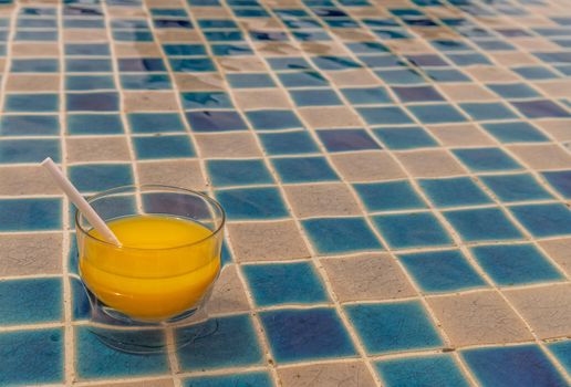 A glass of fresh orange juice for a refreshment on swiwming pool. Outdoor swimming pool background.