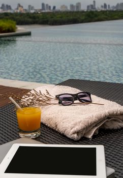 Relaxing moment by the pool. Take a break from working on laptop and tablet and enjoy the fresh orange juice for a refreshment.  Outdoor swimming pool background. leisure activity.