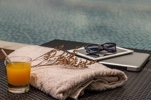Relaxing moment by the pool. Take a break from working on laptop and tablet and enjoy the fresh orange juice for a refreshment.  Outdoor swimming pool background. leisure activity.