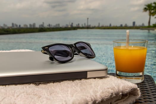 Relaxing moment by the pool. Take a break from working on laptop and enjoy the fresh orange juice for a refreshment.  Outdoor swimming pool background. leisure activity.