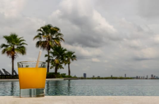 Relaxing moment by the pool. Take a break from enjoy the fresh orange juice for a refreshment. Outdoor swimming pool background. leisure activity.