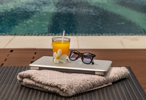 Relaxing moment by the pool. Take a break from working on laptop and enjoy the fresh orange juice for a refreshment.  Outdoor swimming pool background. leisure activity.