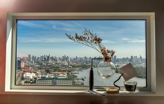 Relaxing area by the window and city views with coffee cup, dried flower vase. City view, Copy space.