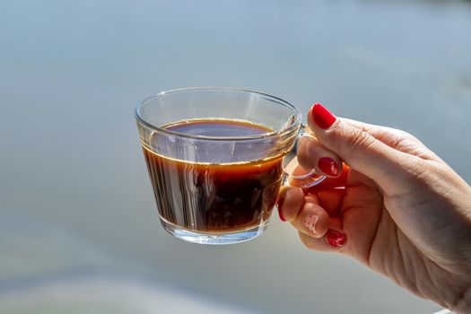 Hand of woman Holding a coffee glass cup with river views. Copy space.