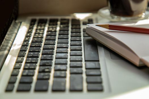 Side view with keyboard laptop, notebook with pencil at comfortable office work table. Creative concept. Selective focus.