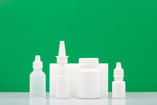 Medication bottles with eye drops, nasal spray, pills and ear drops on white table against green background with copy space. Concept of health care and medication