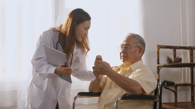 Asian young woman doctor prescribes medicine to older disabled patient on wheelchair when elderly senior man patient's time to go home. Medicine and health care system