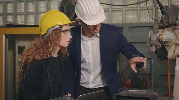 Caucasian maintenance engineer man and diverse female factory workers in hardhats talking and present or explain robot welding machine on plant, Manager supervisor and industrial manufacturing