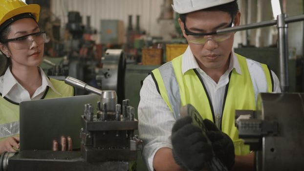 Asian professional mechanical engineer woman and operation man wearing uniform hardhat and goggles safety working on workshop metal lathe industrial manufacturing factory, Heavy industry lathe worker