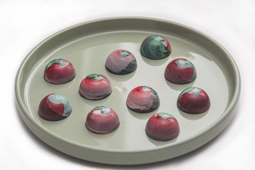 Collectible handmade tempered chocolate sweets with a glossy painted body on a round plate with blur elements. Stock photography.