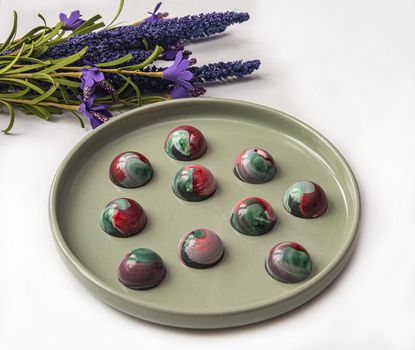 Collectible handmade tempered chocolate sweets with a glossy painted body on a round plate. Stock photography.