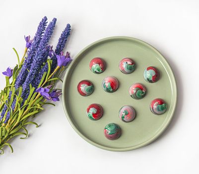 Collectible handmade tempered chocolate sweets with a glossy painted body on a round plate with blur elements. View from above. Stock photography.