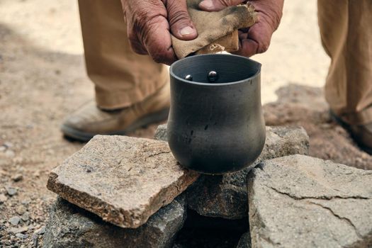 Hands of an adult man pouring hot coffee from a turk into a metal mug